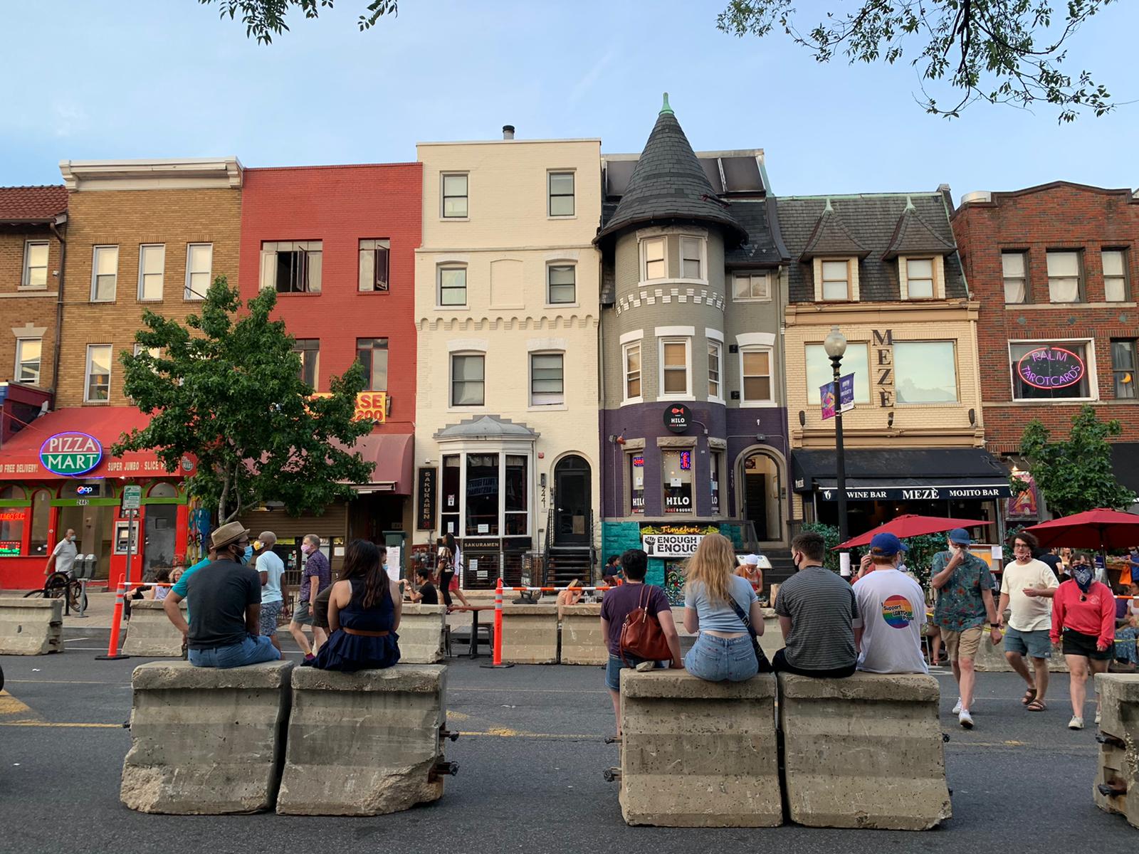 People sitting on concrete barriers alongside outdoor restaurant