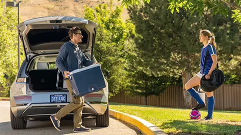 man unloading cooler from back of hybrid car for daughter's soccer game