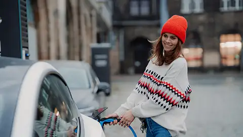 Woman pluggin in electric car in winter