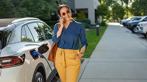 woman talking on the phone outside while charging her parked electric car