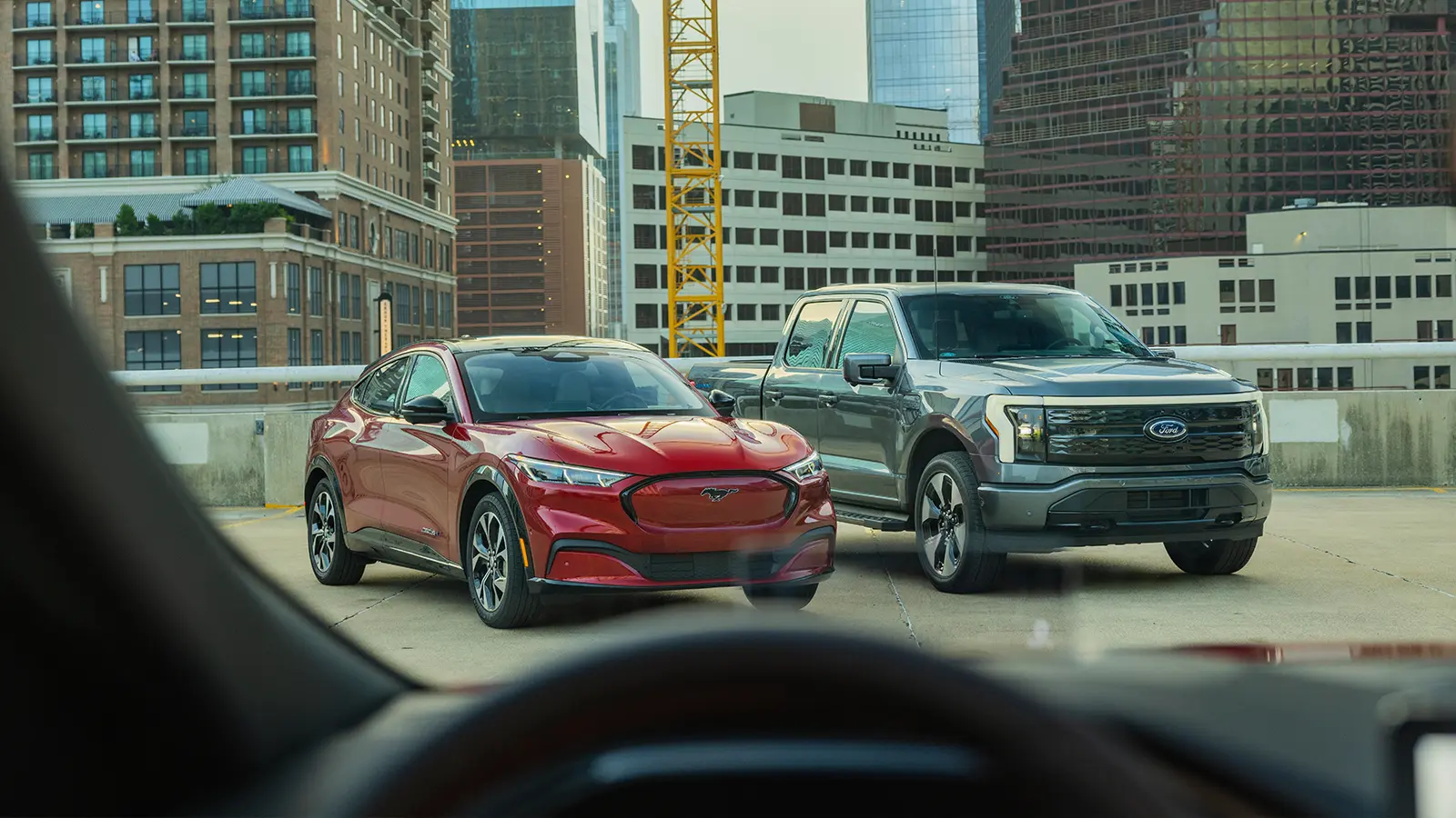 Green Ford F-150 Lightning and Red Mustang Mach-E on display by cityscape 