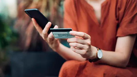 Person making a purchase, holding their phone and credit card.