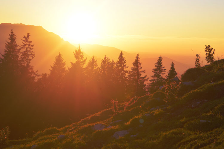 High contrast image of a sun setting behind the mountains.