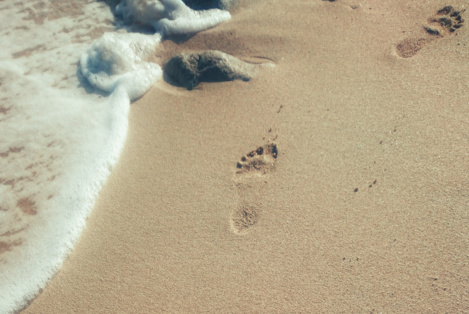 A carbon footprint being symbolized by footprints in the sand on a beach.