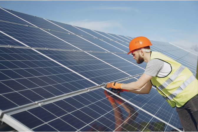 Man in orange hardhat leaning over a large bank of solar panels