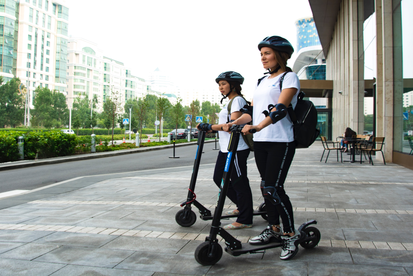 Two people on electric scooters carrying bags
