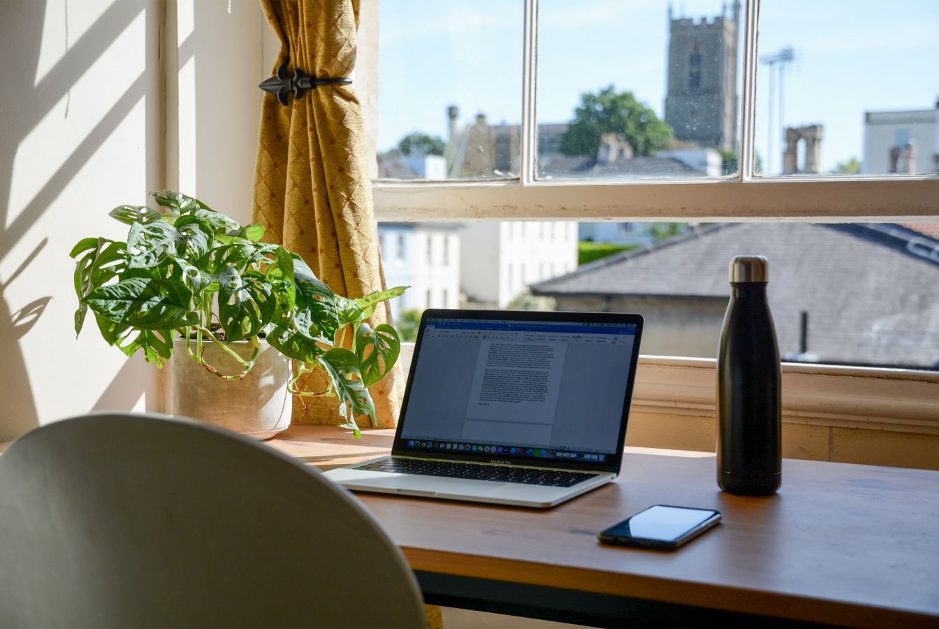 Laptop computer on a desk facing a window that is half open