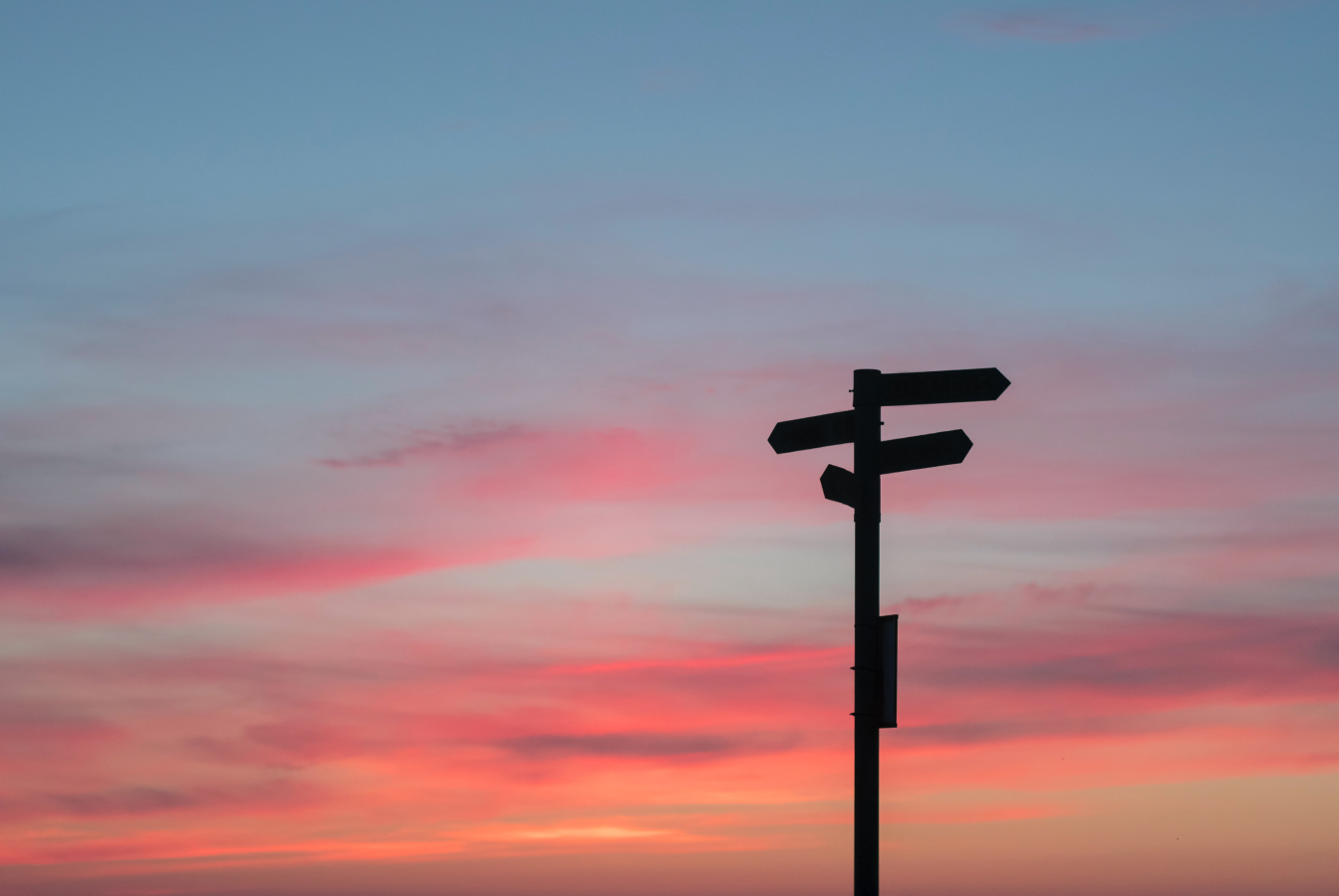 A signpost pointing in multiple directs against a sunset sky