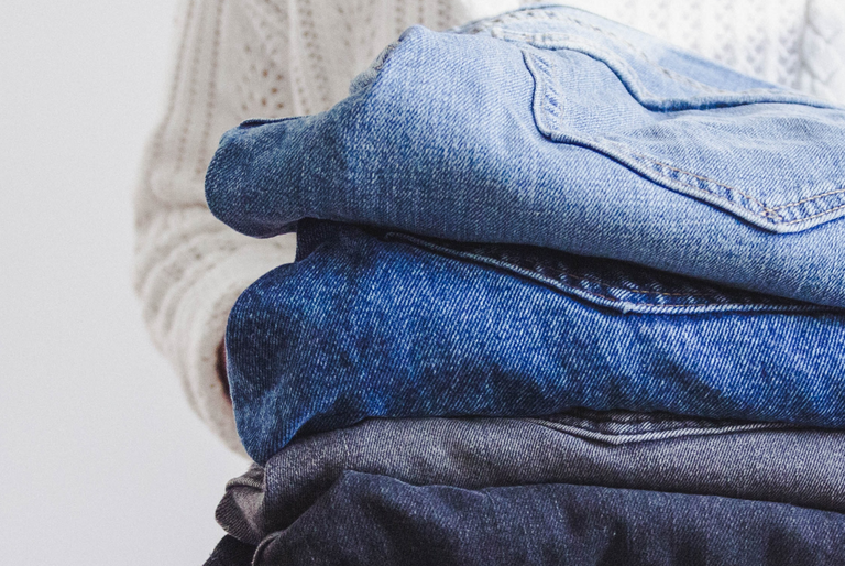 A person holds a pile of well-worn jeans in different washes