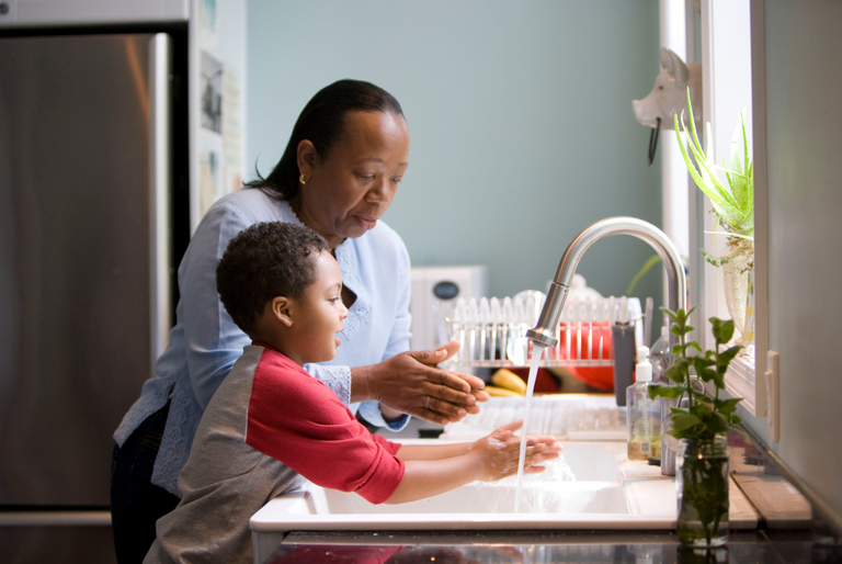 A woman and child hand wash dishes in the kitchen to reduce their carbon footprint at home