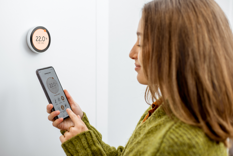 A woman uses her smart phone to set the temperature on her home's thermostat