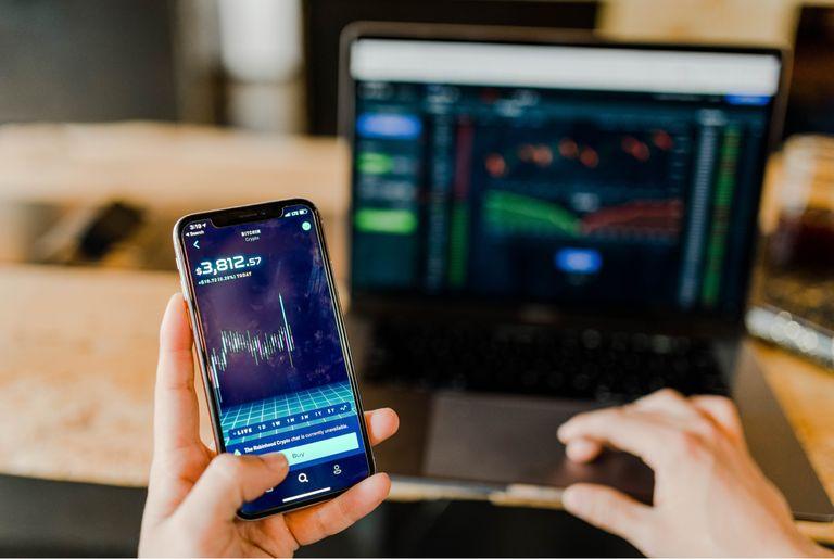 A crypto trader using a laptop and mobile phone to see the price of Bitcoin