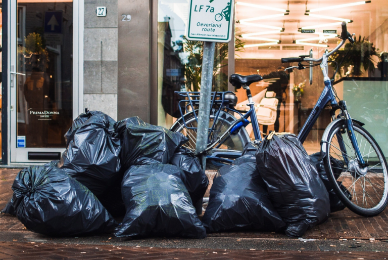 Black garbage bags filled with trash overflowing the side of a city street