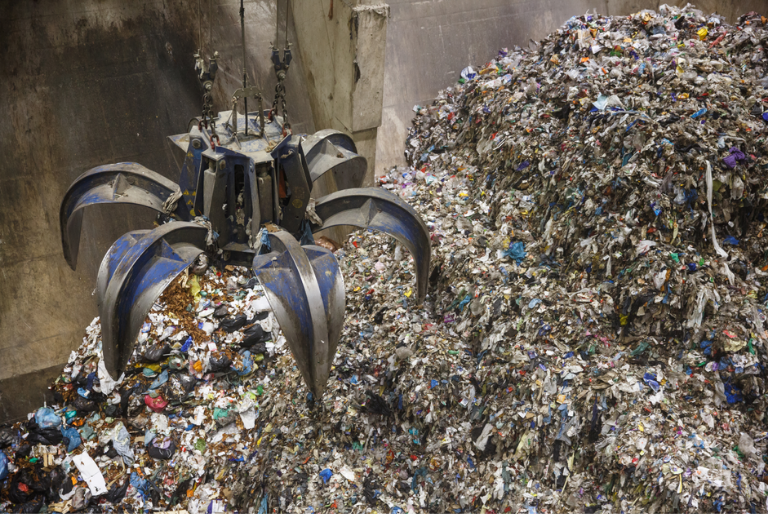 An excavator claw grabbing trash at an industrial landfill