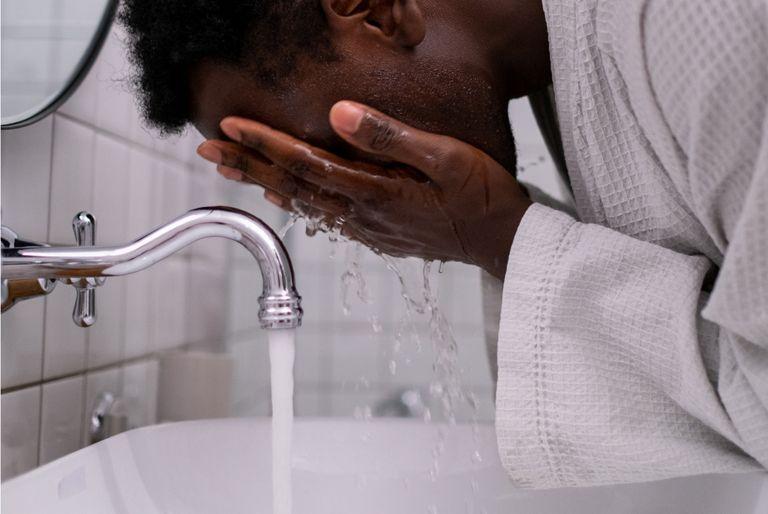 Man splashing water on his face while leaving the tap running
