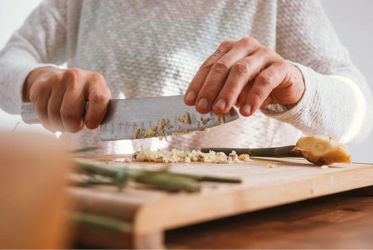 A person chopping raw ginger for a sustainable, vegan dish
