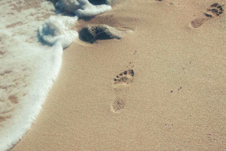 A carbon footprint being symbolized by footprints in the sand on a beach.