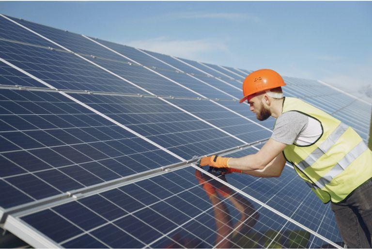 Man in orange hardhat leaning over a large bank of solar panels, which were funded by a carbon offset project.