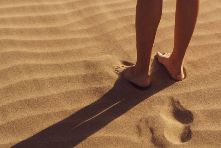 A human leaving footprints behind in the sand symbolizing a human's carbon footprint.