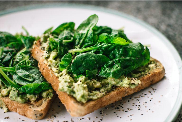 A healthy vegan meal including avocado toast topped with spinach on a plate.