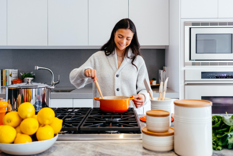 A woman cooks on her stove with an orange cast iron pan