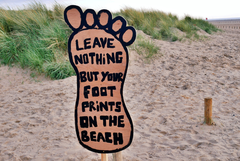 A sign on a beach that reads Leave Nothing But Your Footprints