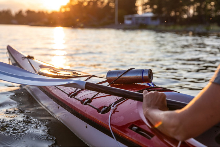A reusable water bottle is strapped to a kayak on the water