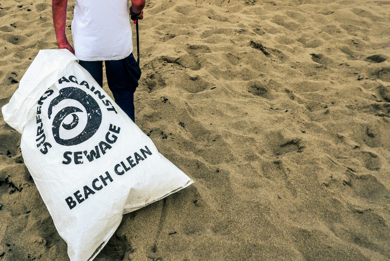 A person stands next to a full bag at a beach clean