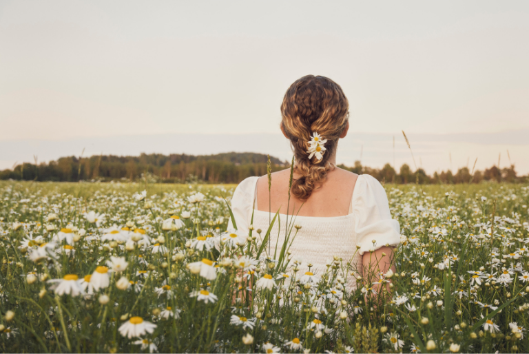 A woman stands in a field of daisies looking out to the horizon
