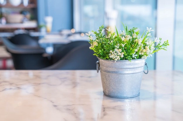 metal bucket with fake plants on marble table