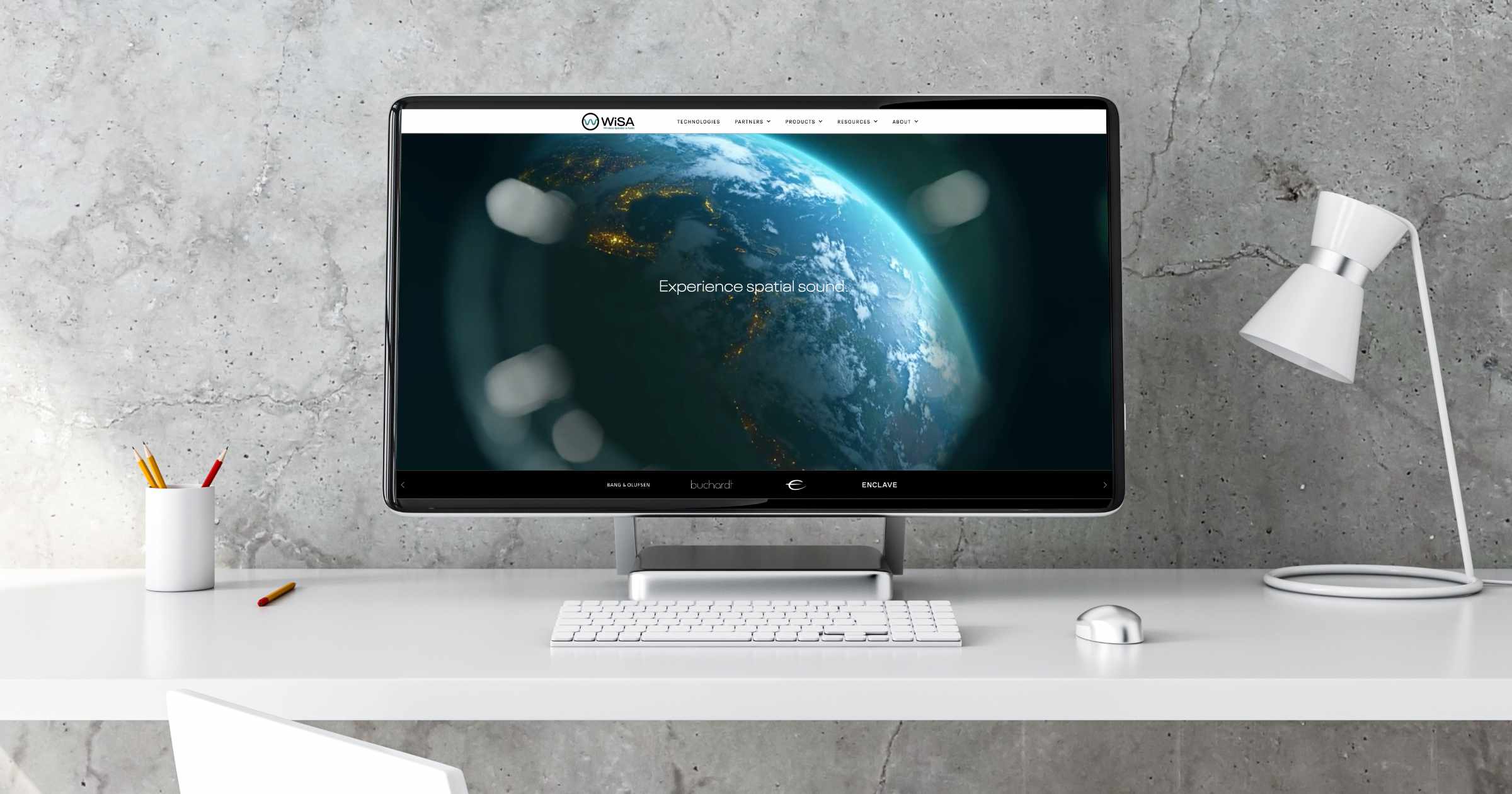 a stone wall, in front of it is a desk with a white lamp and a computer monitor displaying the WiSA website