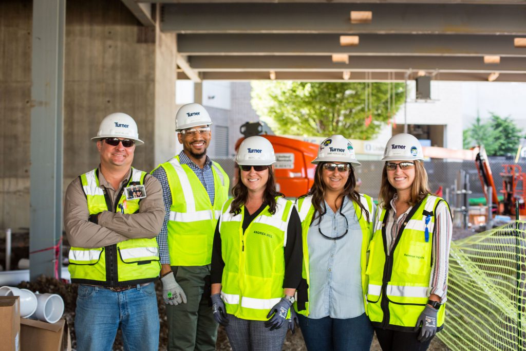 Five construction workers from Turner Construction standing in a line smiling.