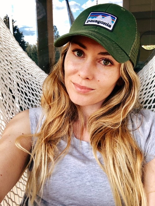 A portrait of me, Juliana Linder. I'm wearing a green Patagonia hat, a grey shirt, looking directly into the camera with a closed smile.