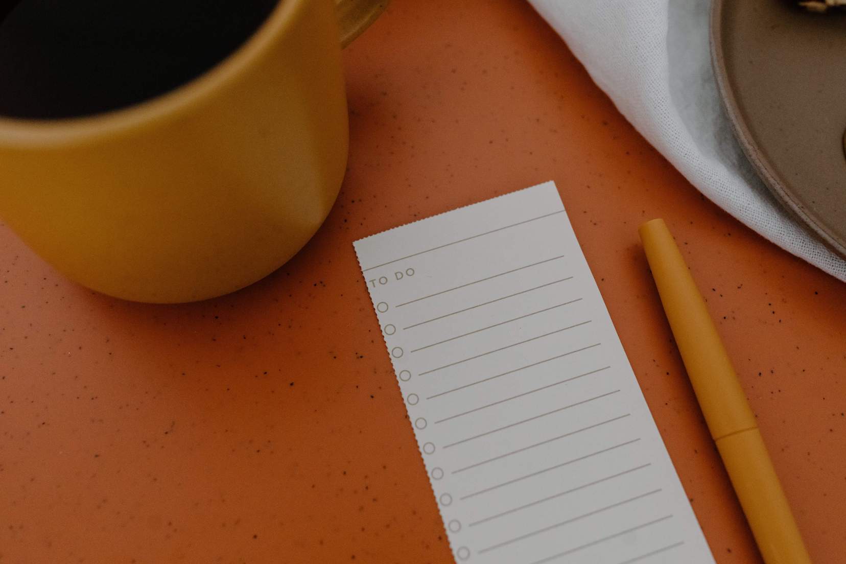 Orange coffee cup on an orange table with a to-do list and orange pen