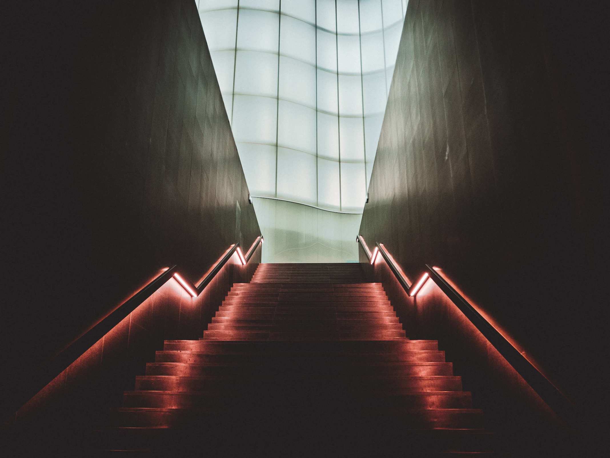 A dark staircase lit with pastel pink lights leading to a gigantic window