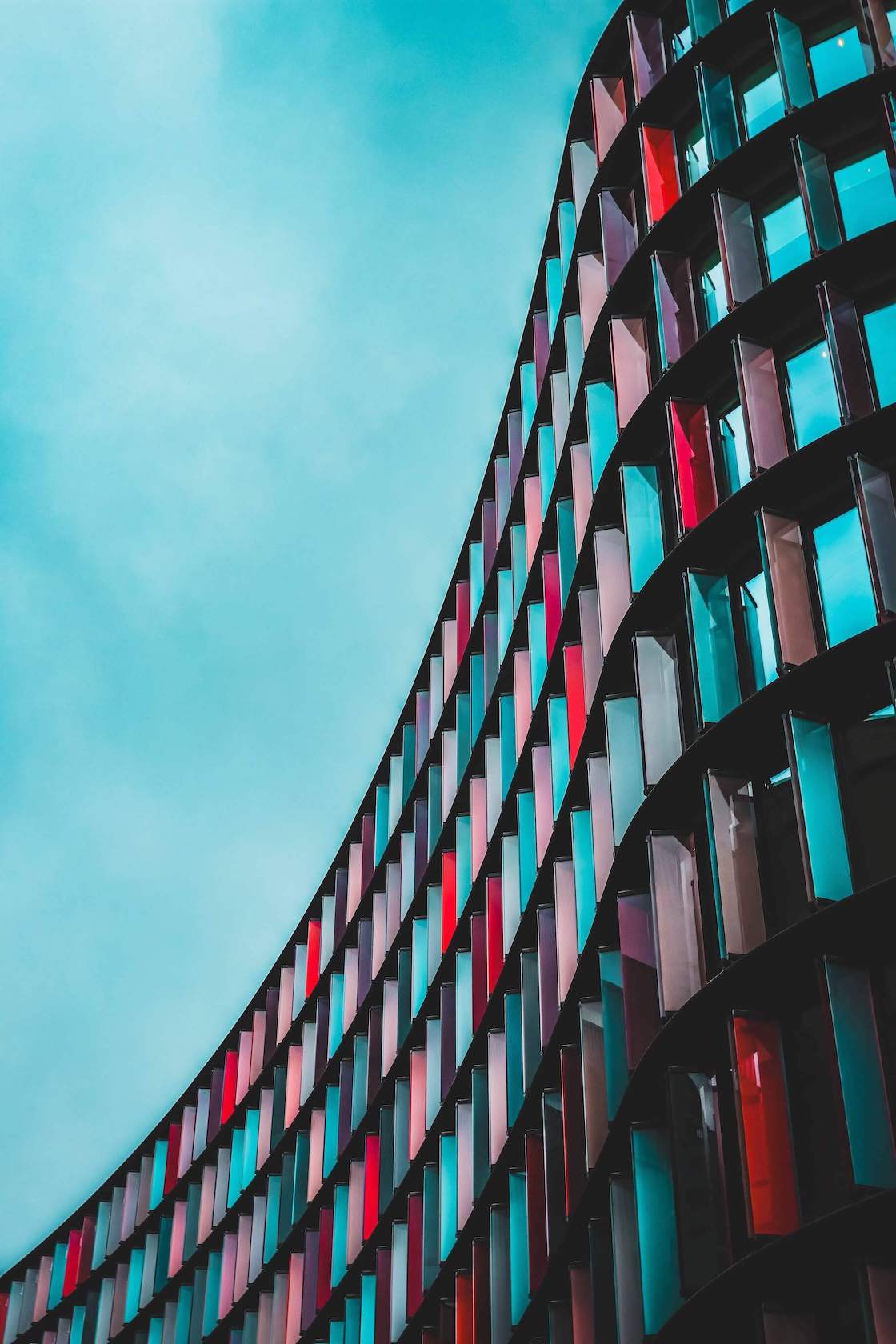 A curved building with blue and red-colored windows set against a blue sky