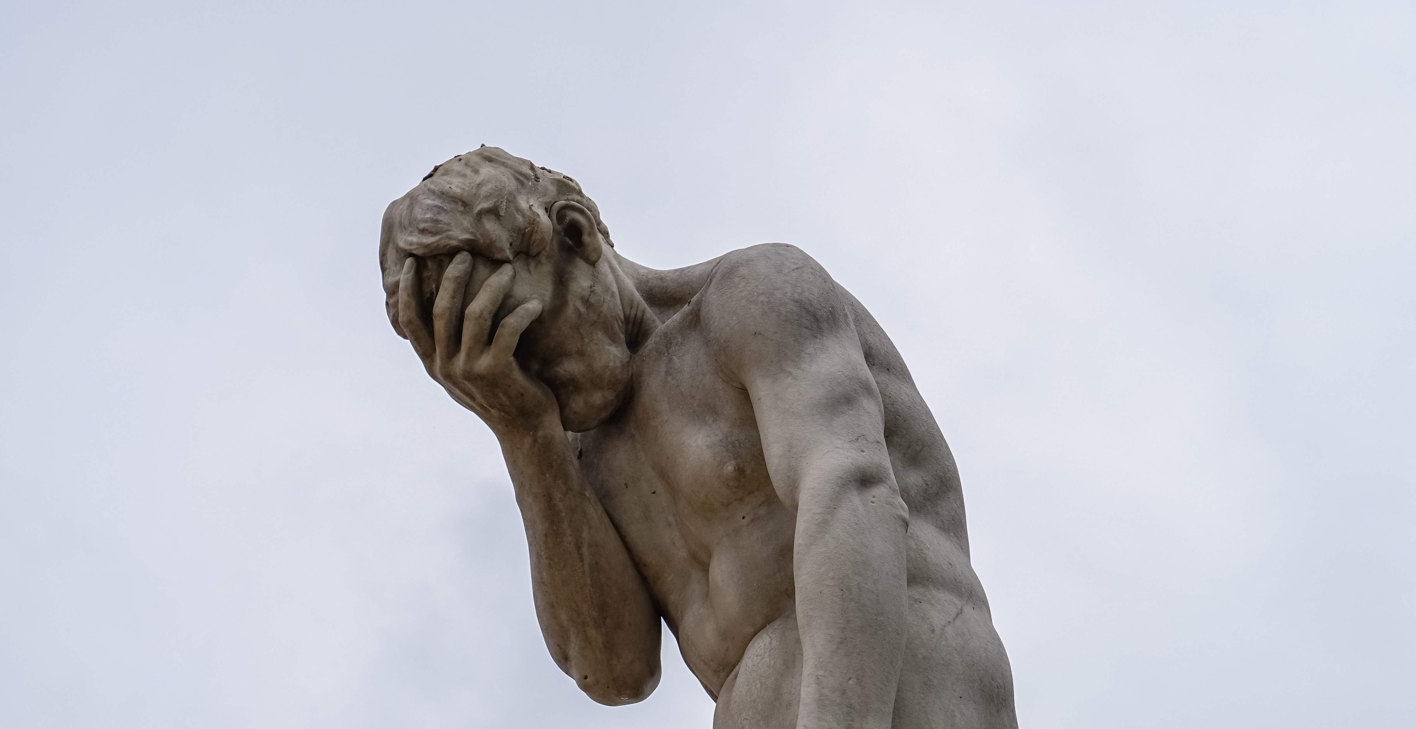 An ancient stone outdoor statue of a man who appears to be doing a facepalm.