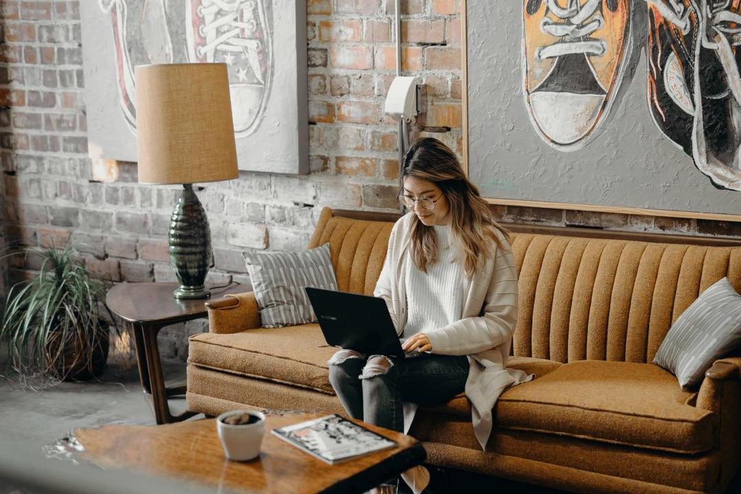 A female hybrid workplace employee working on her computer on a couch in the office.
