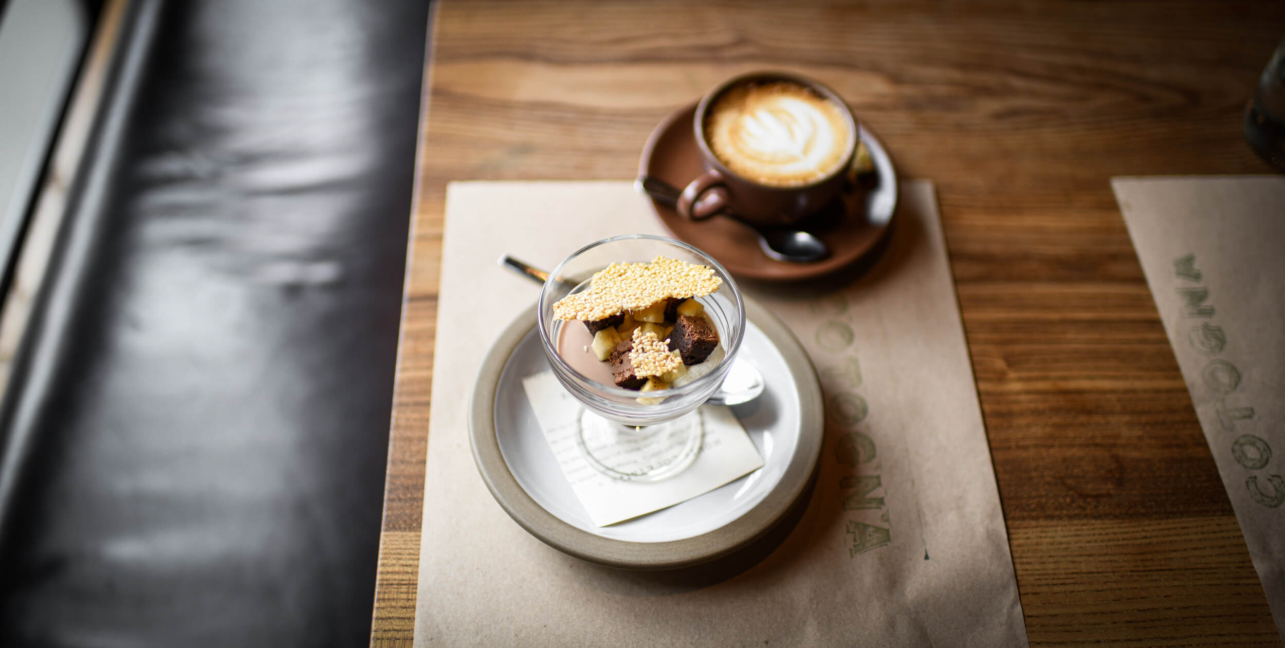 a bowl of dessert sitting next to a cup of cappuccino
