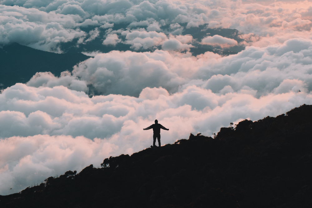 A man standing with arms outstretched, with beautiful clouds in the background