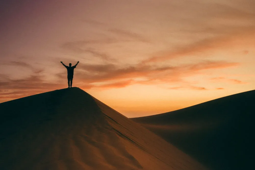 A man at sunset, standing with his hands raised and praising God