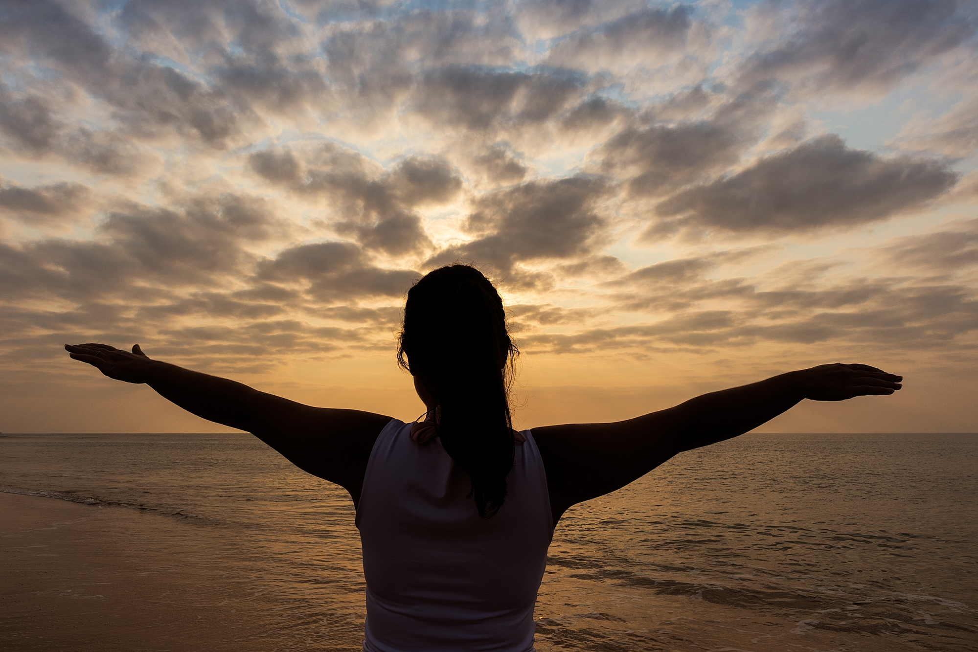 Woman' silhouette with arms spread out in front of the sunset 