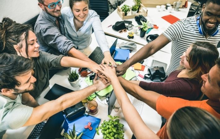 A group of young employees place their hands in a circle in a sign of comradery