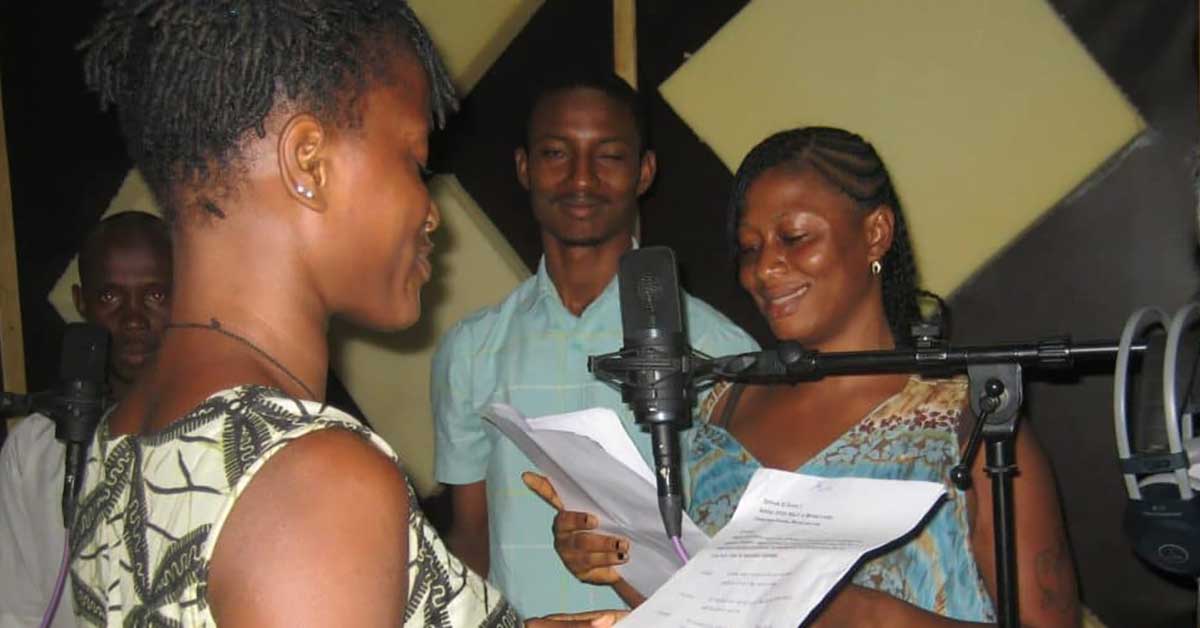 Two women look at their script pages while in front of a microphone 