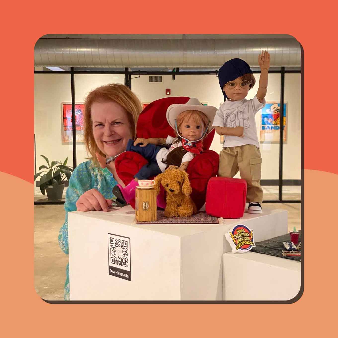 A woman with red hair smiles next to two dolls