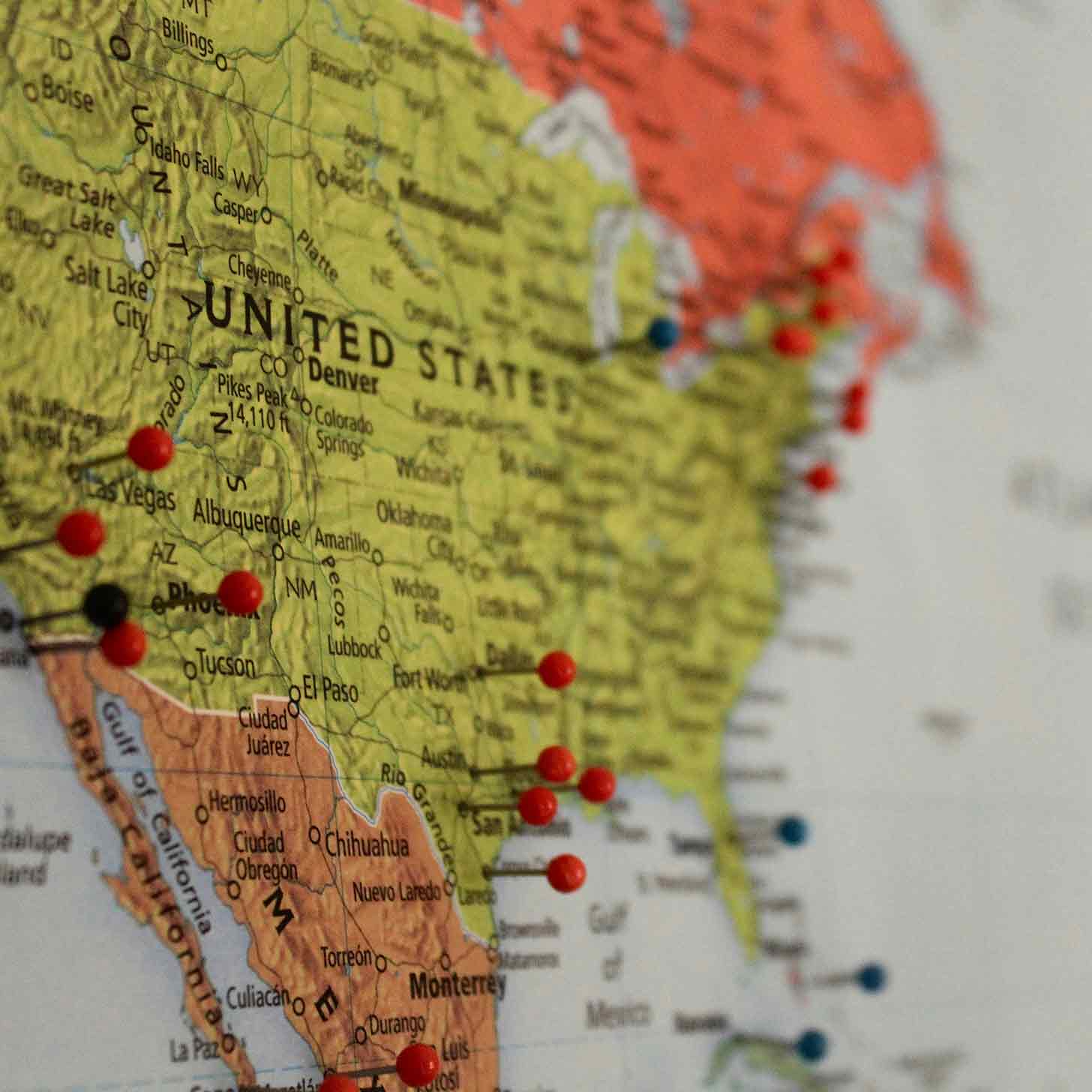 An up-close photo of a map of the United States of America with pin markers scattered all over its surface