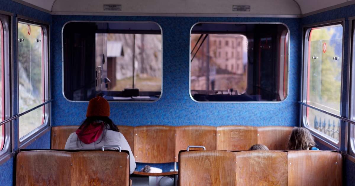 A female train passenger sits on a wooden seat on a train traveling through the French countryside. 