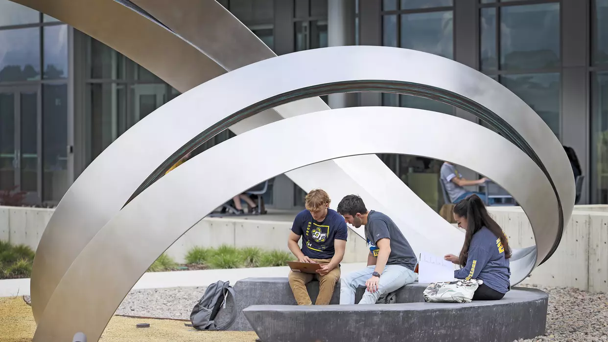 Students sitting on a bench, looking over a laptop screen, at the Oregon Institute of Technology