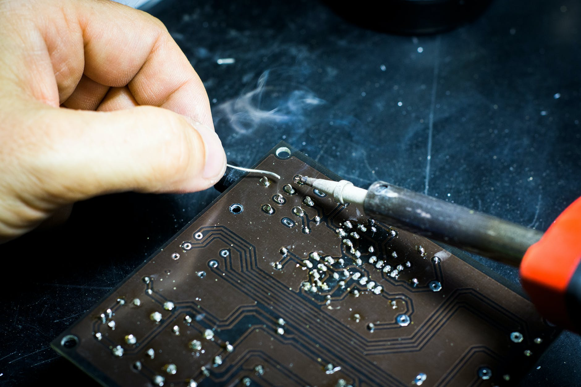 Technician soldering circuits on electrical board