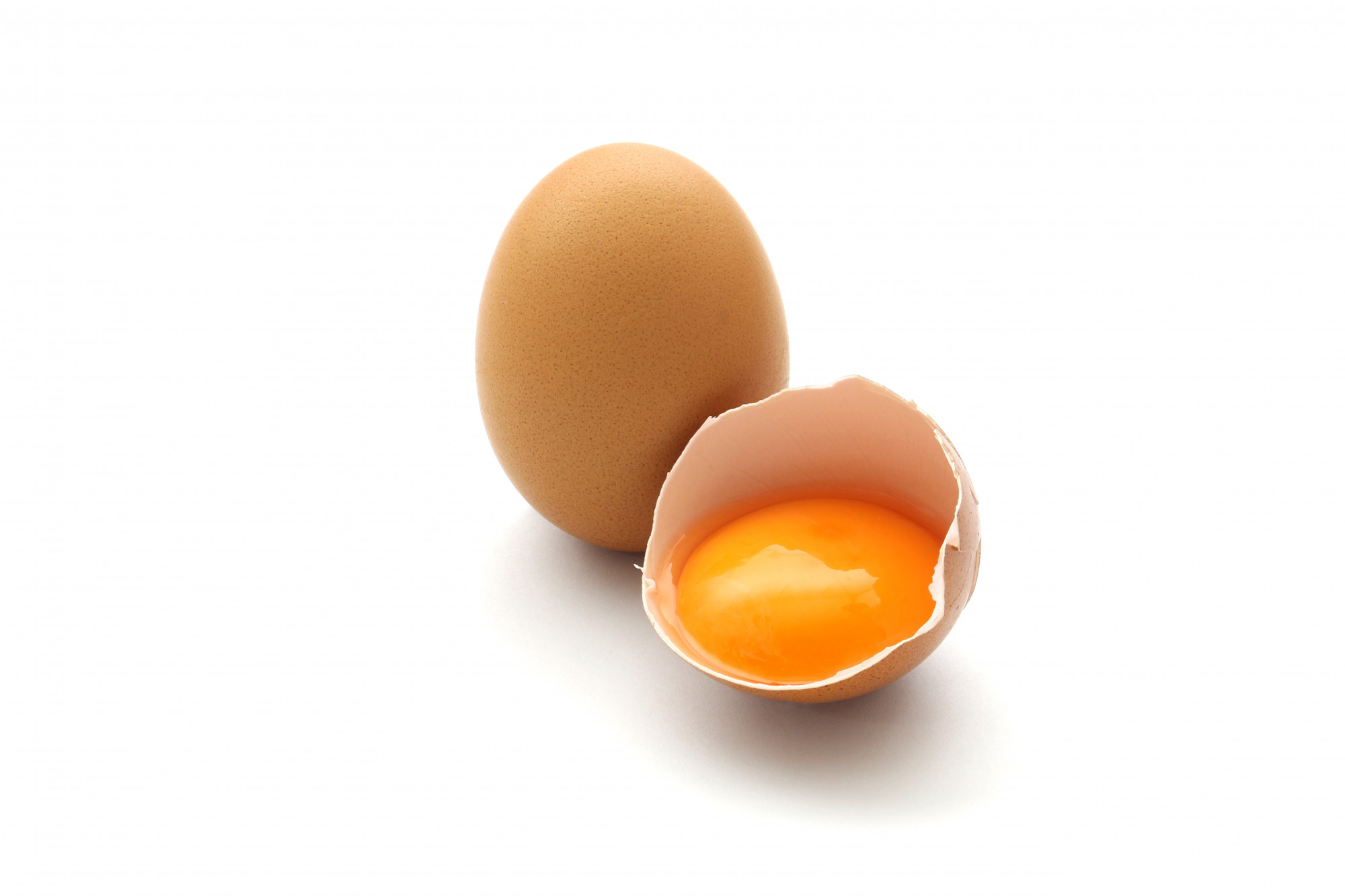 One whole brown egg beside cracked brown egg that has exposed yolk